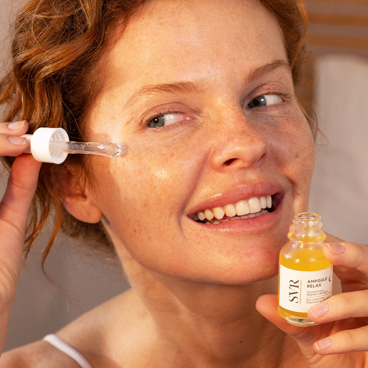 Kobieta aplikuje serum SVR Ampoule Relax za pomocą szklanej pipety na skórę wokół oczu.