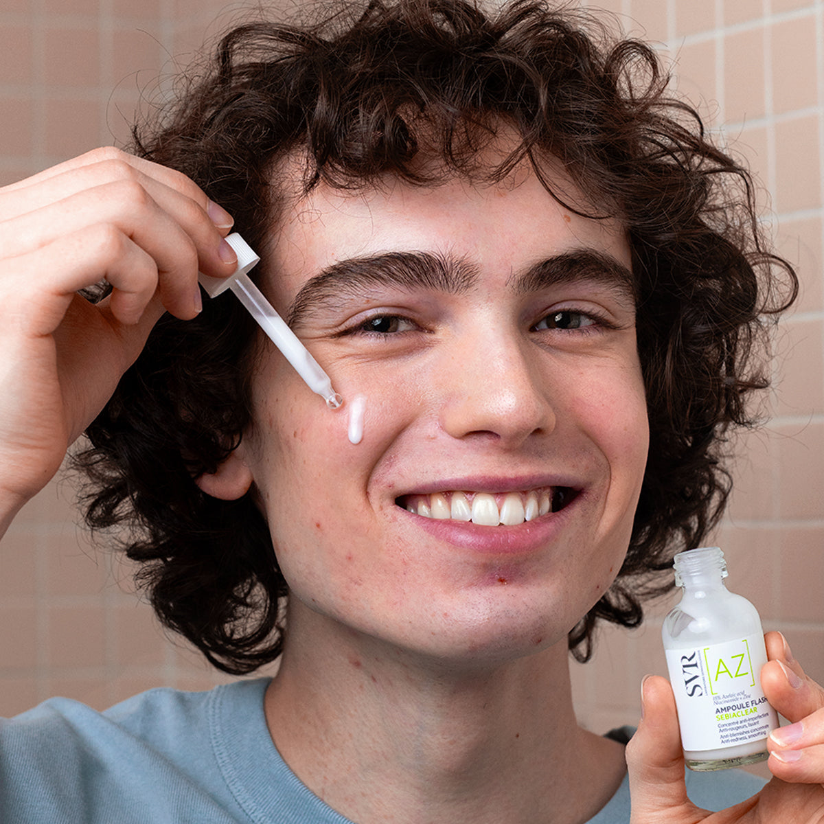 Młody mężczyzna nakłada białe serum SVR Sebiaclear Ampoule AZ Flash na twarz za pomocą szklanej pipety.