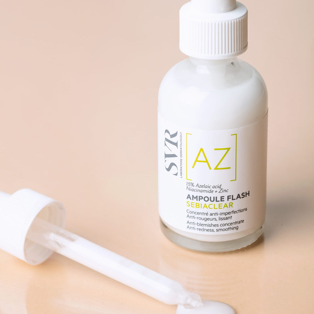 Szklana butelka serum SVR Sebiaclear Ampoule AZ z białą pipetą na beżowym tle, widoczne napisy i mleczna konsystencja.
