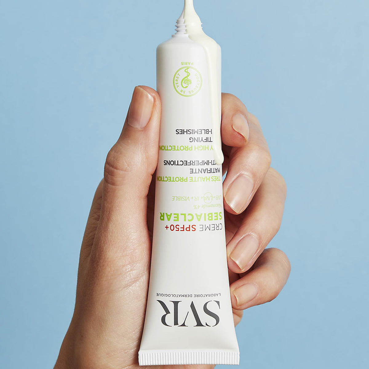 Dłoń trzymająca białą tubkę kremu SVR Sebiaclear SPF50+ z wyciśniętą na górze kremową konsystencją produktu.