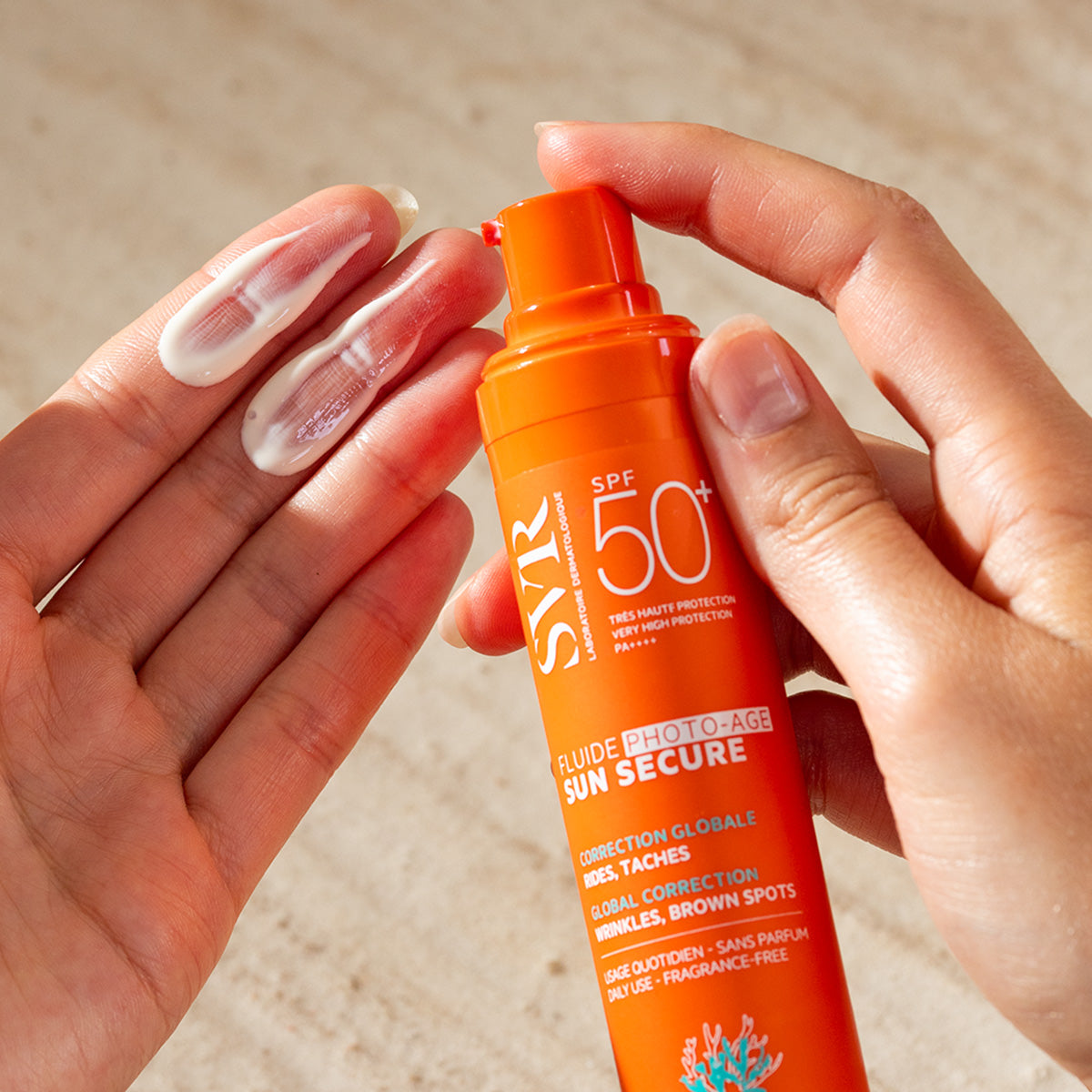 Hands holding an orange SVR SUN SECURE SPF50+ pump bottle with white sunscreen cream dispensed on fingers.